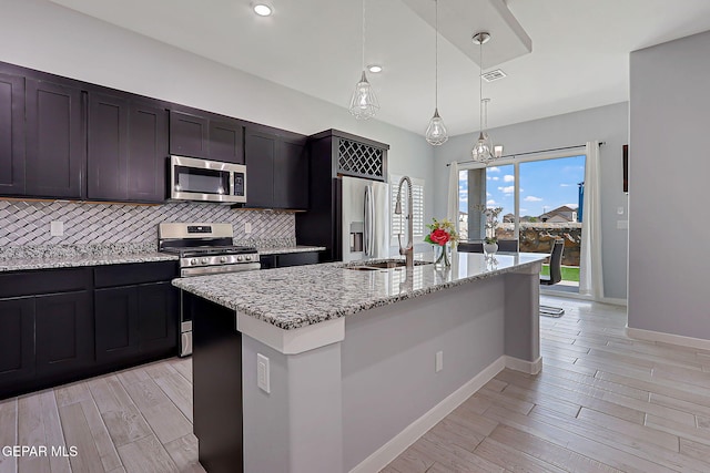 13860 Summer View Ave, El Paso, TX 79928 - kitchen featuring appliances with stainless steel finishes, tasteful backsplash, light stone countertops, a kitchen island with sink, and light wood-type flooring