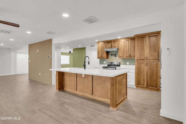 10229 Luella Ave, El Paso, TX 79925 - kitchen with stainless steel range, light wood-type flooring, light countertops, under cabinet range hood, and tasteful backsplash