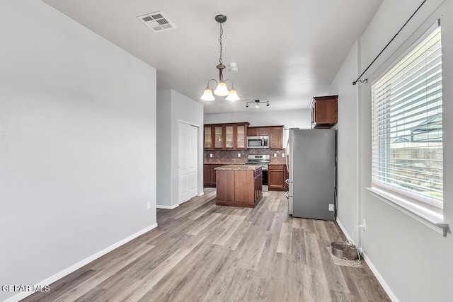 12879 Hidden Grove Dr, El Paso, TX 79938 - kitchen featuring appliances with stainless steel finishes, a kitchen island, decorative backsplash, and light wood-style flooring