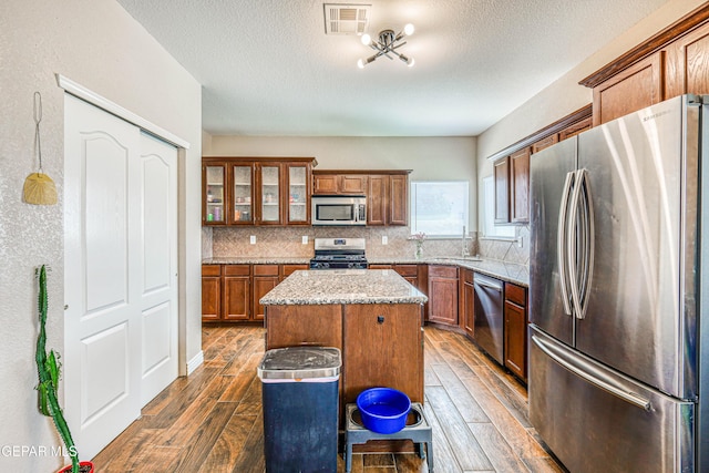 401 Everlook Ln, Horizon City, TX 79928 - kitchen featuring appliances with stainless steel finishes, dark wood-style floors, brown cabinets, a kitchen island, and tasteful backsplash