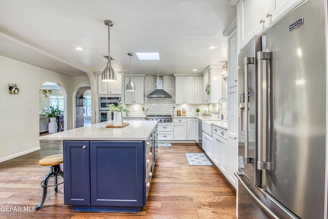 5430 Davis Cup Ct, El Paso, TX 79932 - kitchen featuring appliances with stainless steel finishes, wall chimney range hood, arched walkways, white cabinetry, and a kitchen island