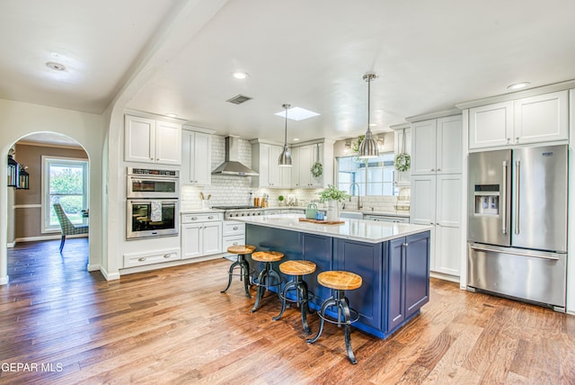 5430 Davis Cup Ct, El Paso, TX 79932 - kitchen featuring appliances with stainless steel finishes, wall chimney range hood, arched walkways, light countertops, and light wood-type flooring