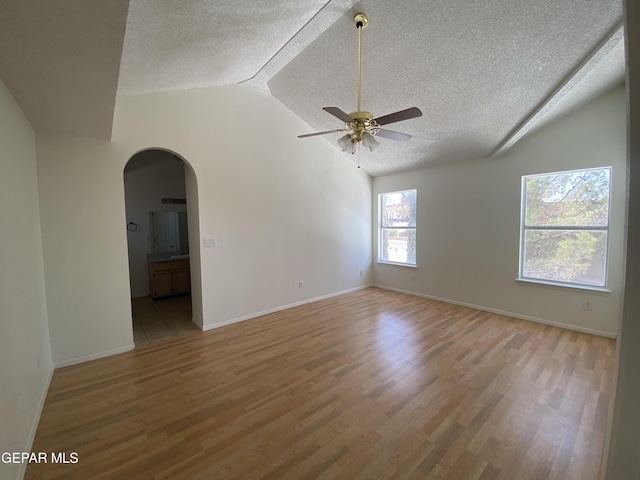 1409 Rainbow Ridge Dr, El Paso, TX 79912 - spare room featuring a textured ceiling, vaulted ceiling, arched walkways, light wood-style floors, and ceiling fan