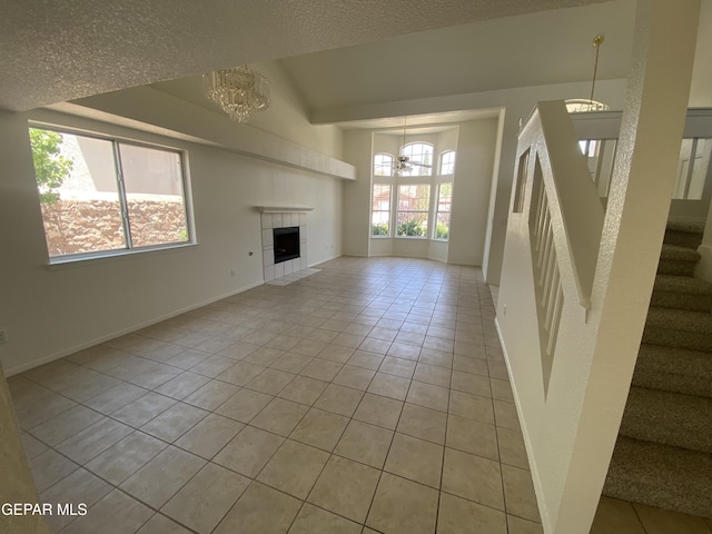 1409 Rainbow Ridge Dr, El Paso, TX 79912 - unfurnished living room with a chandelier, light tile patterned floors, stairway, a textured ceiling, and a tiled fireplace