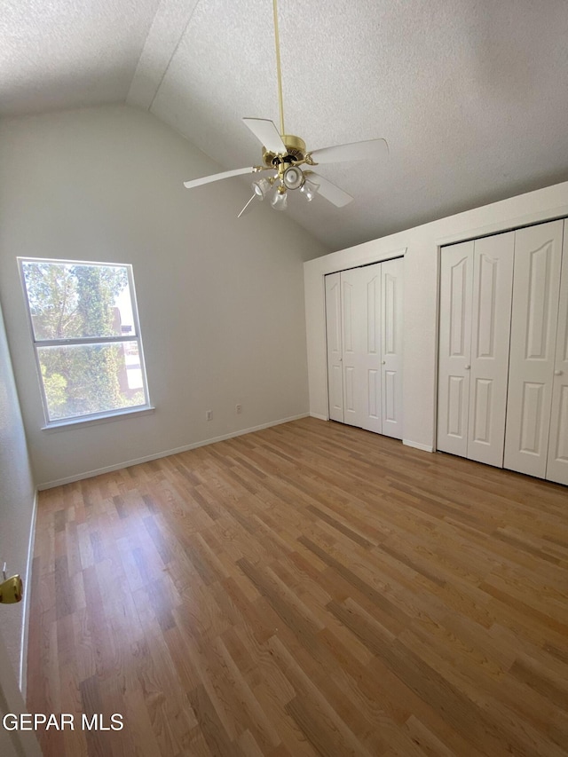 1409 Rainbow Ridge Dr, El Paso, TX 79912 - unfurnished bedroom with lofted ceiling, light wood-style flooring, two closets, a textured ceiling, and ceiling fan