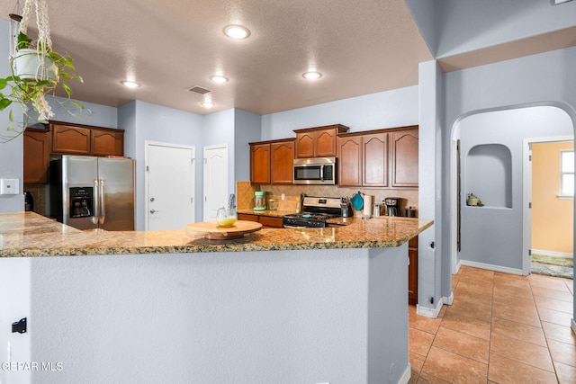 14605 Spanish Point Dr, El Paso, TX 79938 - kitchen with appliances with stainless steel finishes, backsplash, arched walkways, light stone countertops, and a textured ceiling