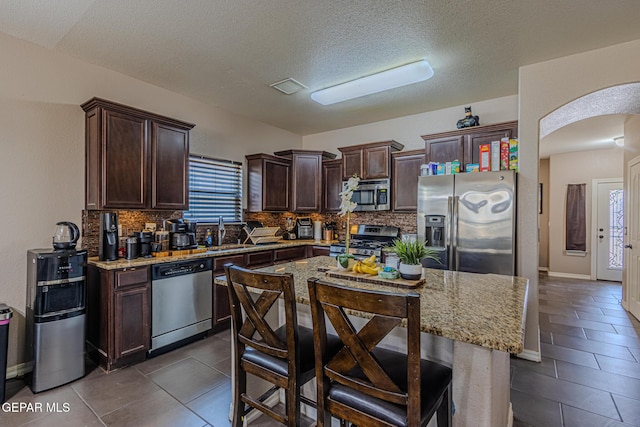 12355 Joe Gomez, El Paso, TX 79928 - kitchen with stainless steel appliances, arched walkways, dark brown cabinetry, backsplash, and a textured ceiling