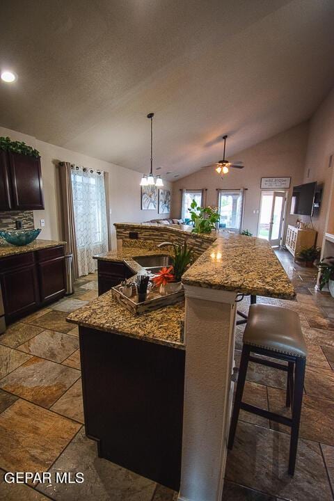 11344 Acoma St, El Paso, TX 79934 - kitchen with lofted ceiling, a kitchen island with sink, stone tile floors, ceiling fan, and a kitchen bar