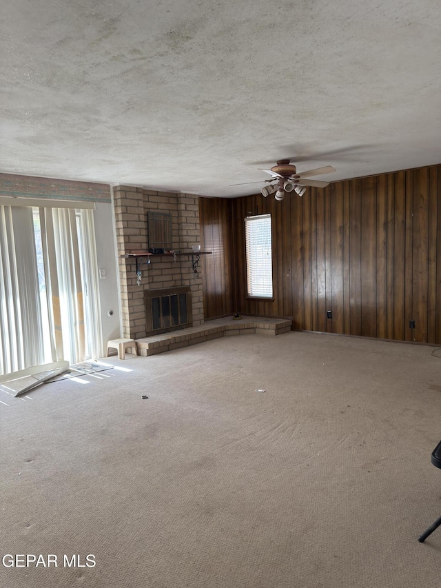 3376 Guthrie St, El Paso, TX 79935 - unfurnished living room with plenty of natural light, carpet floors, a textured ceiling, a brick fireplace, and wood walls