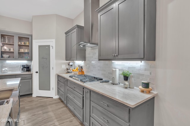 737 Al Smith Ln, El Paso, TX 79932 - kitchen with wall chimney range hood, stainless steel gas cooktop, gray cabinetry, tasteful backsplash, and light wood-style floors