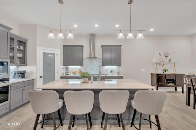 737 Al Smith Ln, El Paso, TX 79932 - kitchen with gray cabinets, wall chimney exhaust hood, decorative backsplash, a kitchen bar, and a kitchen island with sink