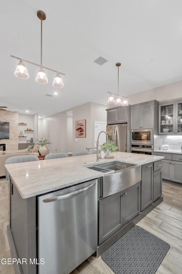 737 Al Smith Ln, El Paso, TX 79932 - kitchen featuring gray cabinets, appliances with stainless steel finishes, an island with sink, light stone counters, and glass insert cabinets