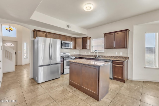 14330 Woods Point Ave, El Paso, TX 79938 - kitchen featuring stainless steel appliances, a kitchen island, arched walkways, light stone counters, and light tile patterned floors