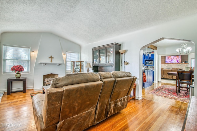 4327 Oxford Ave, El Paso, TX 79903 - living area featuring a large fireplace, arched walkways, light wood-style floors, lofted ceiling, and a textured ceiling