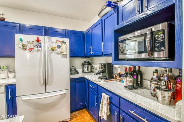 4327 Oxford Ave, El Paso, TX 79903 - kitchen with freestanding refrigerator, stainless steel microwave, blue cabinetry, and light wood-style floors