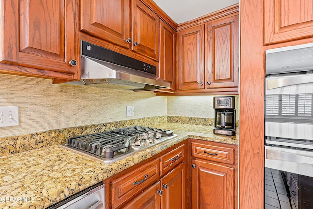 745 Rinconada Ln, El Paso, TX 79932 - kitchen featuring under cabinet range hood, appliances with stainless steel finishes, decorative backsplash, tile patterned flooring, and brown cabinetry