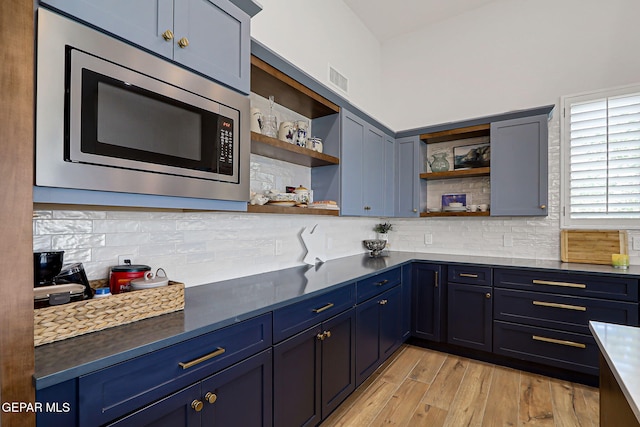 6328 Camino Nogal Dr, El Paso, TX 79932 - kitchen with stainless steel microwave, open shelves, light wood-style floors, backsplash, and blue cabinetry