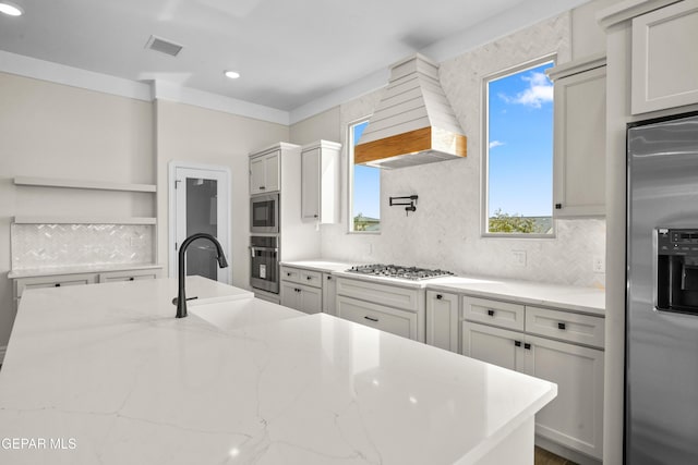 13375 Jeff Winton Dr, El Paso, TX 79928 - kitchen featuring appliances with stainless steel finishes, custom exhaust hood, open shelves, tasteful backsplash, and light stone countertops