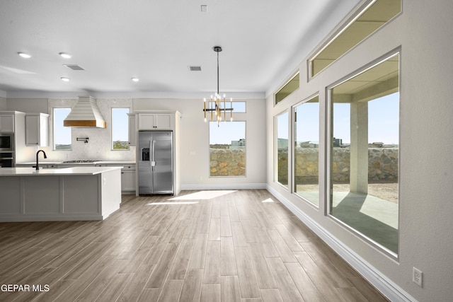 13375 Jeff Winton Dr, El Paso, TX 79928 - kitchen with appliances with stainless steel finishes, custom exhaust hood, light countertops, wood finished floors, and a chandelier