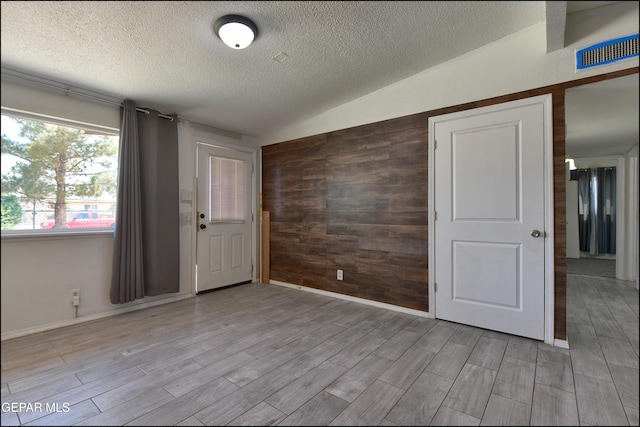 5726 Dearborne Dr, El Paso, TX 79924 - empty room with a textured ceiling, light wood-style floors, vaulted ceiling, and wooden walls