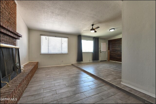 5726 Dearborne Dr, El Paso, TX 79924 - unfurnished living room featuring ceiling fan, a brick fireplace, a textured ceiling, and wood tiled floors