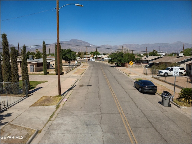 5726 Dearborne Dr, El Paso, TX 79924 - view of asphalt road featuring sidewalks, traffic signs, curbs, a mountain view, and street lights
