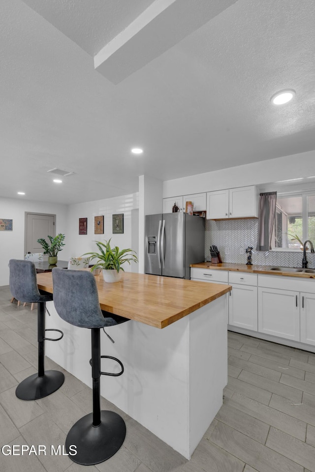 8142 Cook Dr, El Paso, TX 79907 - kitchen featuring butcher block counters, stainless steel fridge, white cabinets, a breakfast bar area, and recessed lighting