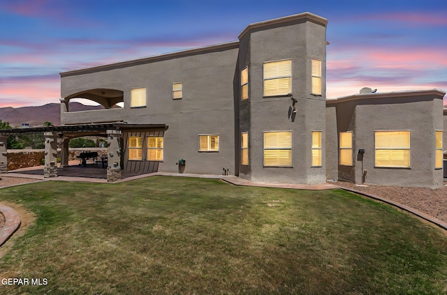 6310 Franklin Crest Dr, El Paso, TX 79912 - back of house at dusk with stucco siding, a lawn, a patio, and a pergola