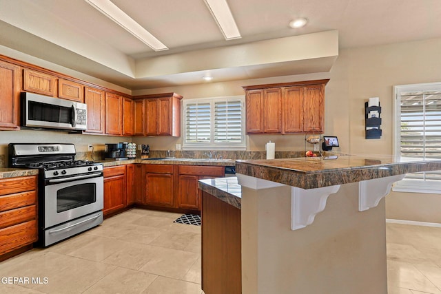 6310 Franklin Crest Dr, El Paso, TX 79912 - kitchen with stainless steel appliances, tile counters, a breakfast bar, brown cabinetry, and light tile patterned flooring