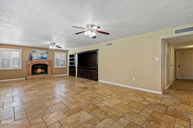 796 Fescue Dr, Canutillo, TX 79835 - unfurnished living room featuring a ceiling fan, a textured ceiling, stone tile flooring, and a warm lit fireplace