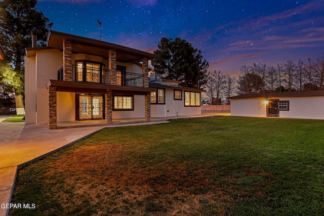 796 Fescue Dr, Canutillo, TX 79835 - back of house at dusk featuring a balcony, stone siding, a yard, french doors, and stucco siding