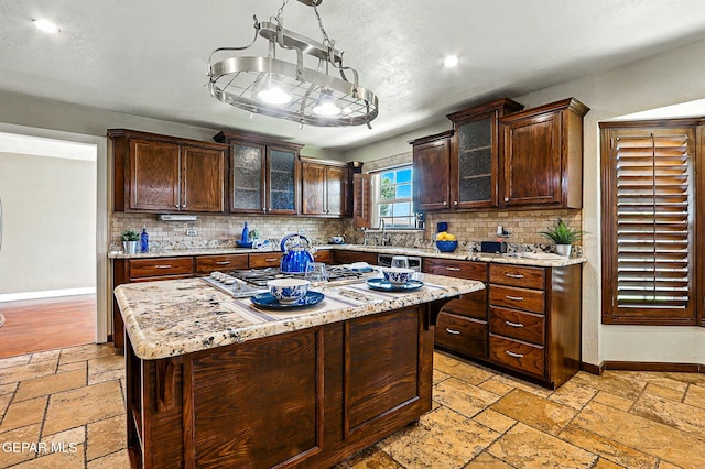 796 Fescue Dr, Canutillo, TX 79835 - kitchen featuring stone tile flooring, tasteful backsplash, stainless steel gas stovetop, a center island, and dark brown cabinets