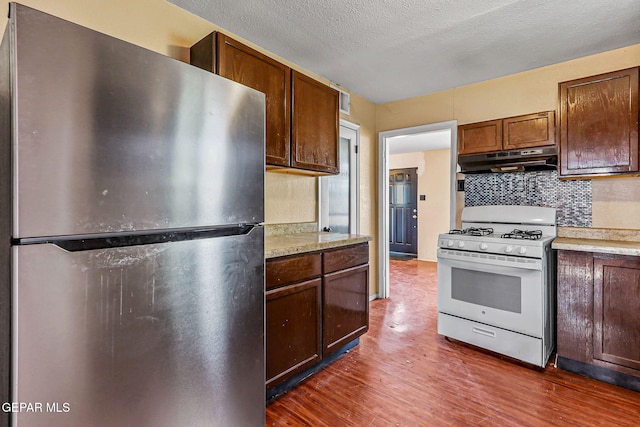 541 Val Verde St, El Paso, TX 79905 - kitchen featuring freestanding refrigerator, white range with gas cooktop, under cabinet range hood, dark wood-type flooring, and light countertops