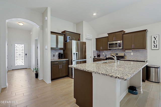 13860 Paseo Sereno Dr, El Paso, TX 79928 - kitchen with stainless steel appliances, arched walkways, dark brown cabinetry, decorative backsplash, and light stone countertops