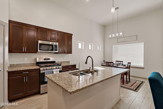 7825 Enchanted View Dr, El Paso, TX 79911 - kitchen with stainless steel appliances, dark brown cabinetry, light stone countertops, hanging light fixtures, and an island with sink