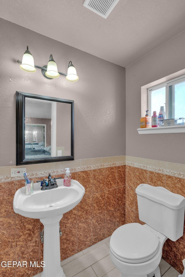 half bath with tile walls, wainscoting, and tile patterned flooring