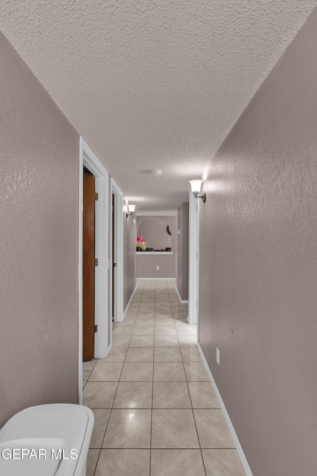 hall featuring light tile patterned flooring and a textured ceiling