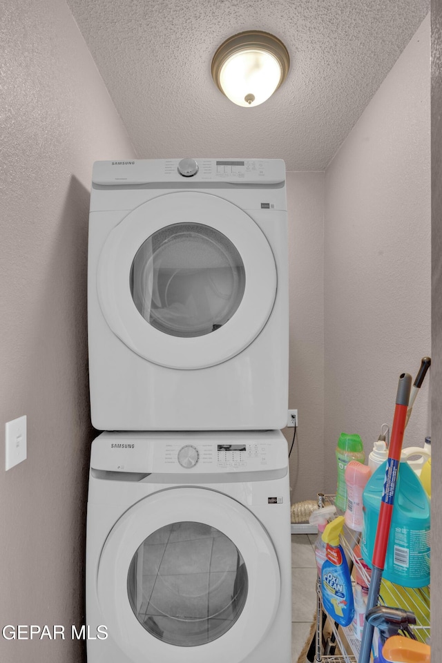 washroom featuring stacked washer / drying machine, a textured ceiling, tile patterned floors, and a textured wall