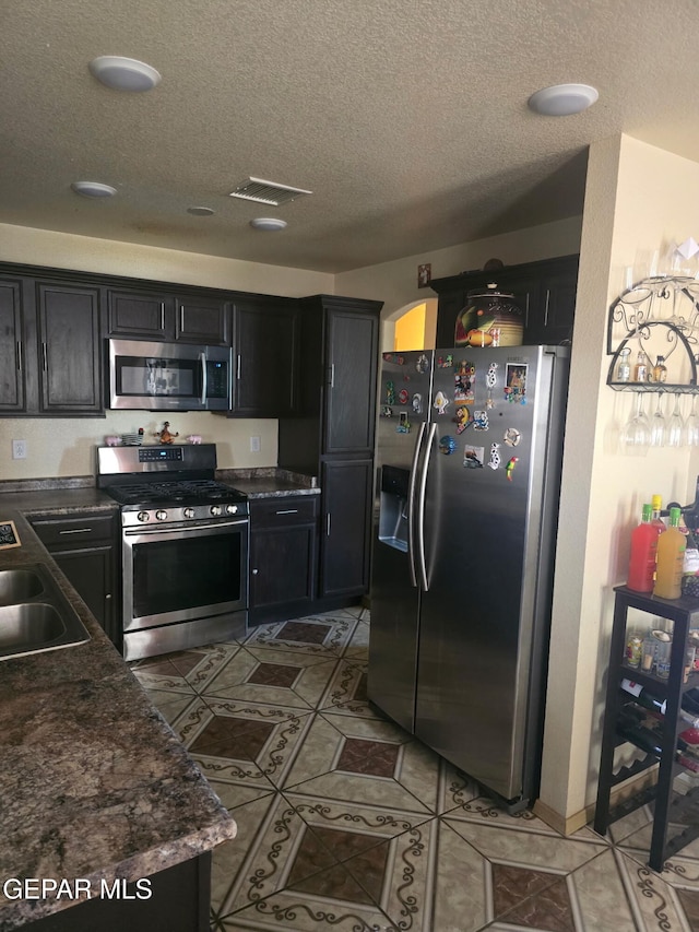 14185 Silver Point Ave, El Paso, TX 79938 - kitchen with stainless steel appliances, a textured ceiling, dark cabinets, light tile patterned floors, and recessed lighting