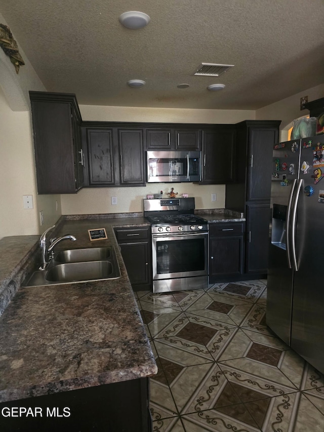 14185 Silver Point Ave, El Paso, TX 79938 - kitchen featuring stainless steel appliances, a textured ceiling, dark countertops, tile patterned flooring, and dark cabinets