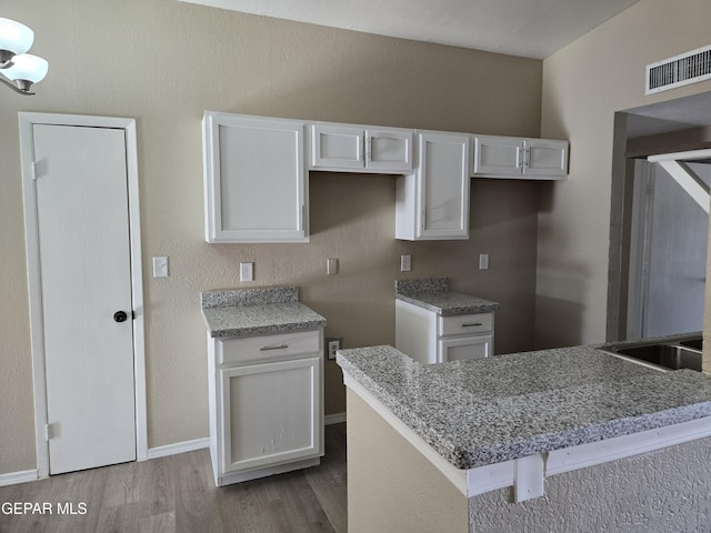 1607 Gene Torres Dr, El Paso, TX 79936 - kitchen with white cabinets, wood finished floors, light stone countertops, and a peninsula