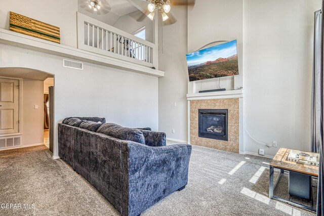 10937 Acoma St, El Paso, TX 79934 - living room with carpet flooring, a high ceiling, a ceiling fan, arched walkways, and a tiled fireplace