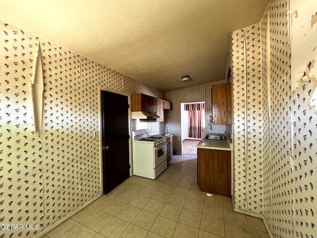 9212 Atun Way, El Paso, TX 79907 - kitchen with wallpapered walls, white gas range, under cabinet range hood, light countertops, and light tile patterned floors