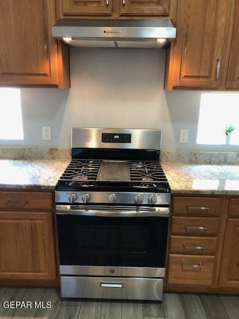 6392 Franklin Gate Dr, El Paso, TX 79912 - kitchen featuring stainless steel range with gas cooktop, range hood, brown cabinetry, light stone counters, and light wood-style floors