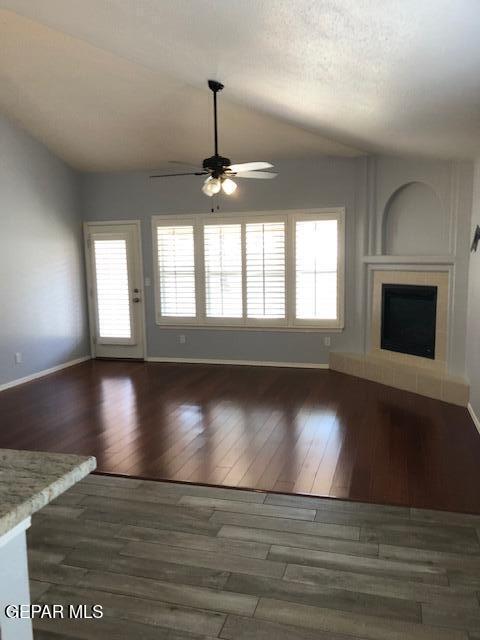 6392 Franklin Gate Dr, El Paso, TX 79912 - unfurnished living room featuring ceiling fan, vaulted ceiling, a fireplace with raised hearth, and wood finished floors