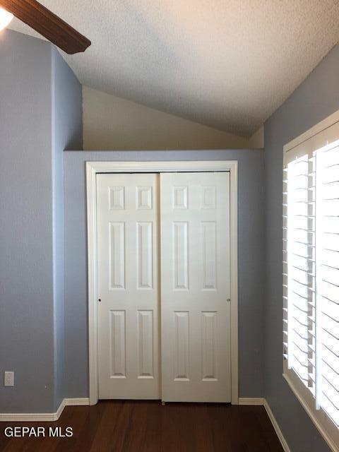 6392 Franklin Gate Dr, El Paso, TX 79912 - unfurnished bedroom featuring lofted ceiling, dark wood-style flooring, multiple windows, a closet, and a textured ceiling