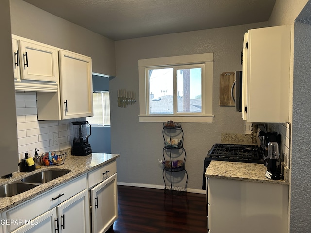1012 Maple St, El Paso, TX 79903 - kitchen with dark wood-style flooring, tasteful backsplash, white cabinets, light stone countertops, and a textured wall