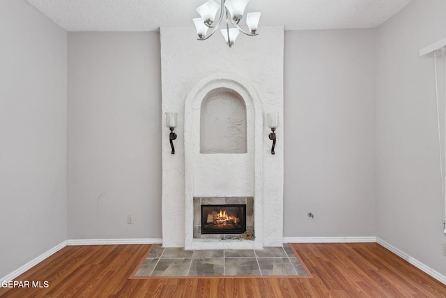 5536 Fernwood Cir, El Paso, TX 79932 - unfurnished living room with a chandelier, wood finished floors, a tiled fireplace, and a textured ceiling