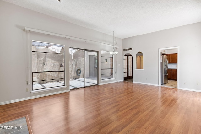 5536 Fernwood Cir, El Paso, TX 79932 - unfurnished living room with light wood finished floors, a chandelier, plenty of natural light, a textured ceiling, and arched walkways