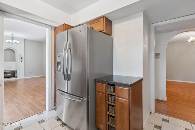 5536 Fernwood Cir, El Paso, TX 79932 - kitchen featuring stainless steel fridge with ice dispenser, a chandelier, arched walkways, brown cabinetry, and a large fireplace